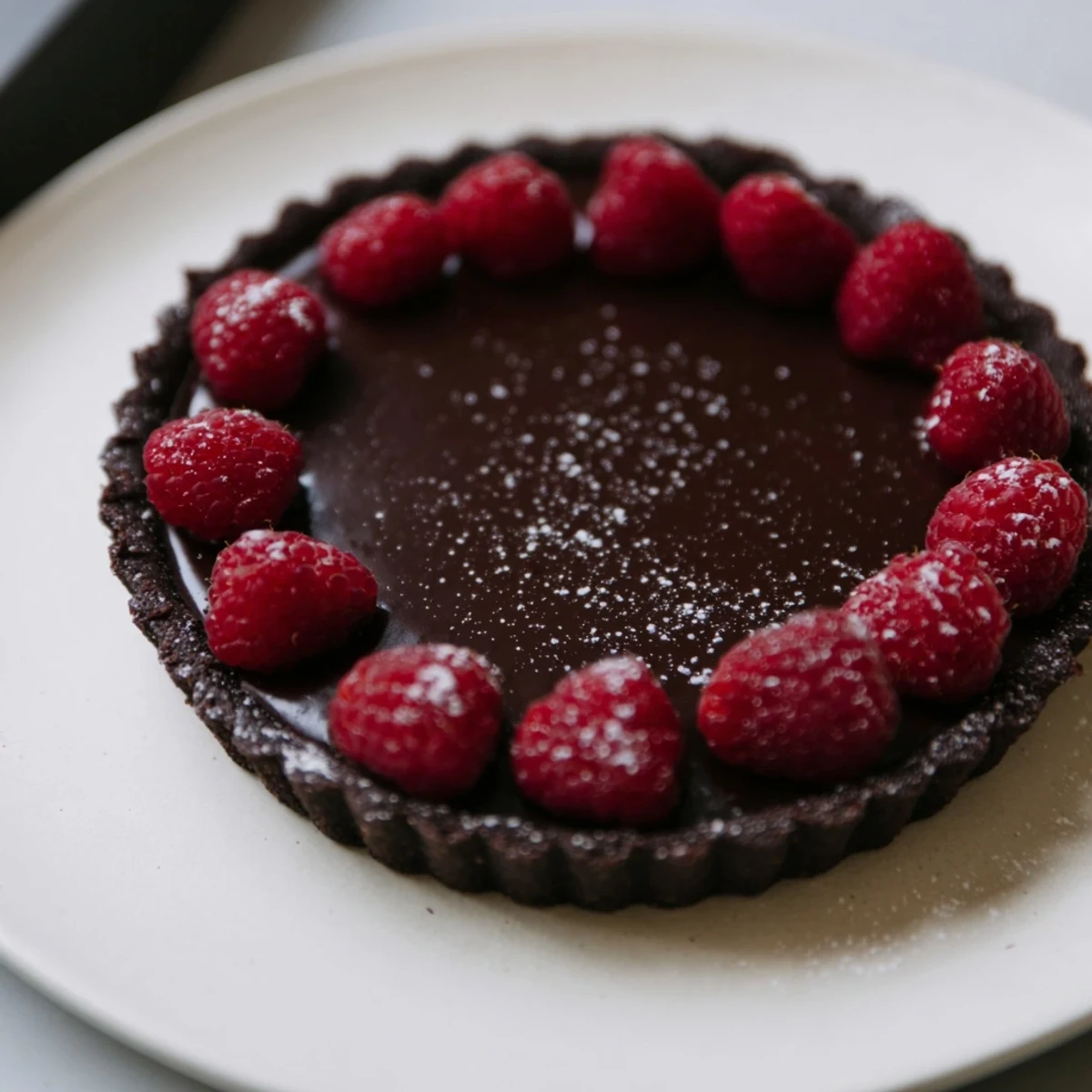 A slice of rich Dark Chocolate and Raspberry Tart, perfect for a special occasion dessert on a plate.