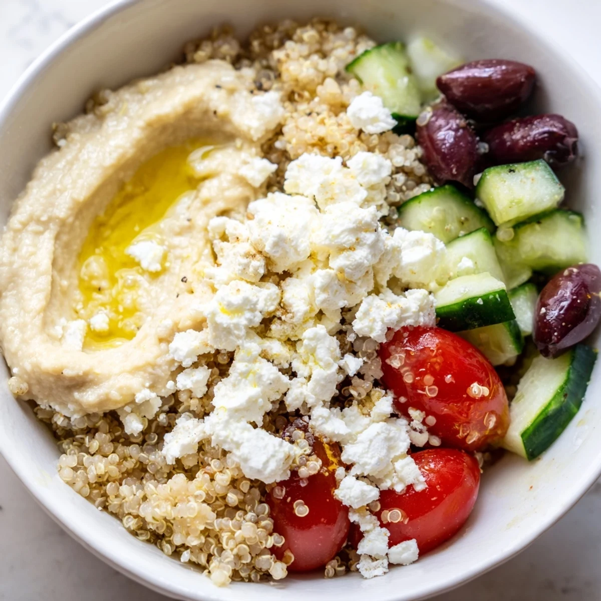 Healthy Mediterranean quinoa bowl with hummus and olives, garnished with parsley and served with lemon wedges.