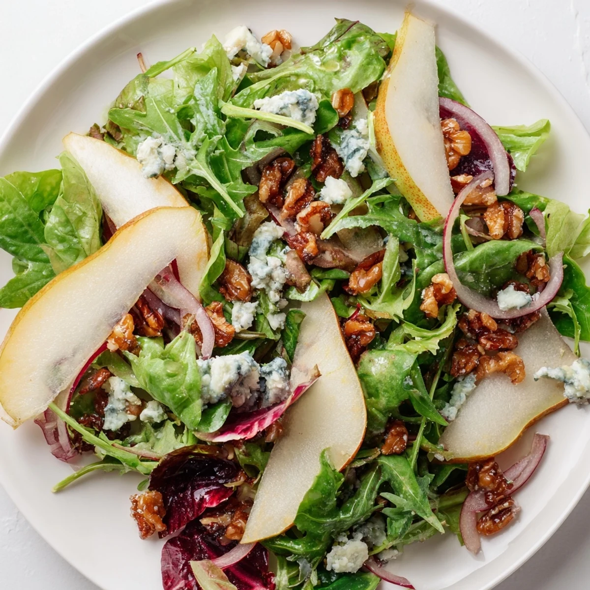 A close-up view of Winter Green Salad with Pear and Candied Walnuts featuring crumbled blue cheese and thin red onion slices.