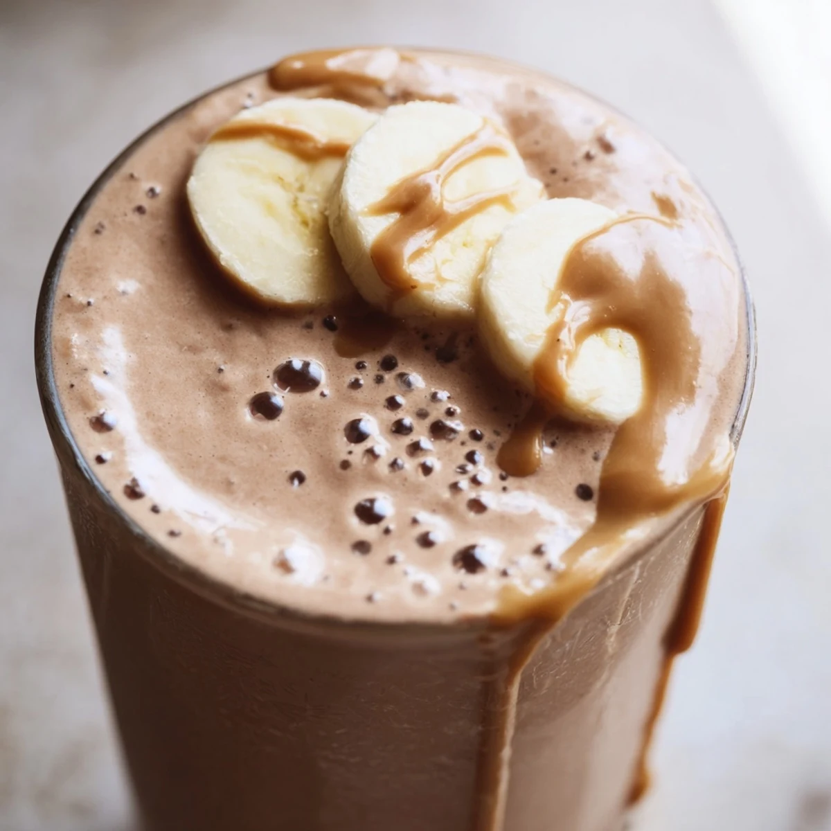 Creamy Chocolate Peanut Butter Smoothie with Banana poured into a tall glass, topped with sliced banana and a peanut butter drizzle.