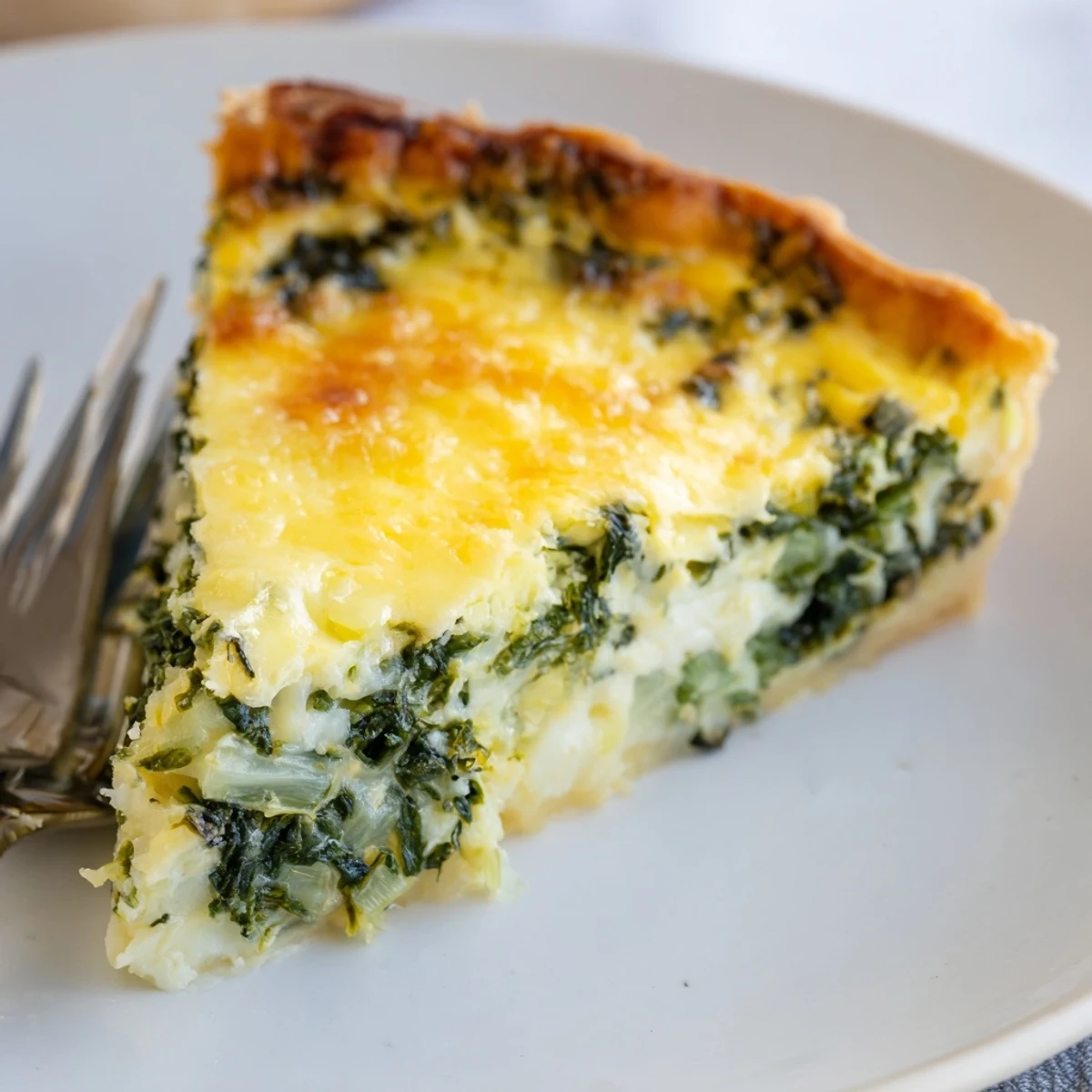 Close-up of a slice of savory quiche with spinach, showing creamy custard.