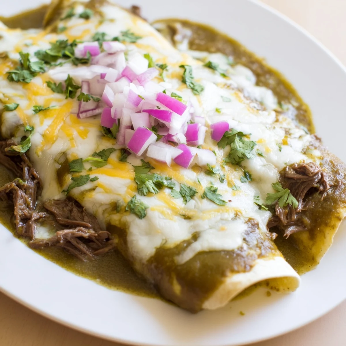 Freshly baked Beef Enchiladas with Green Chili Sauce bubbling in a ceramic dish, garnished with cilantro and red onion.