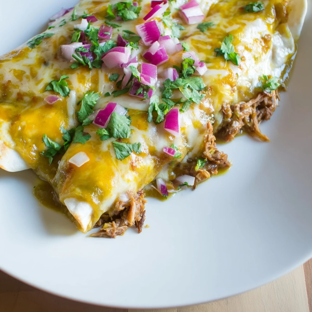 Golden Beef Enchiladas with Green Chili Sauce served on a plate with lime wedges and a side of cilantro.