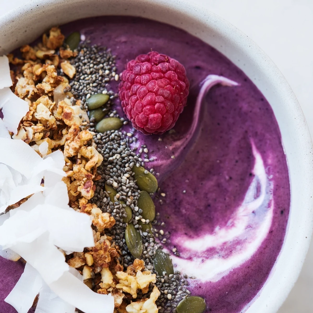 A close-up view of a vibrant Winter Berry Smoothie Bowl topped with seeds, granola, and fresh berries.