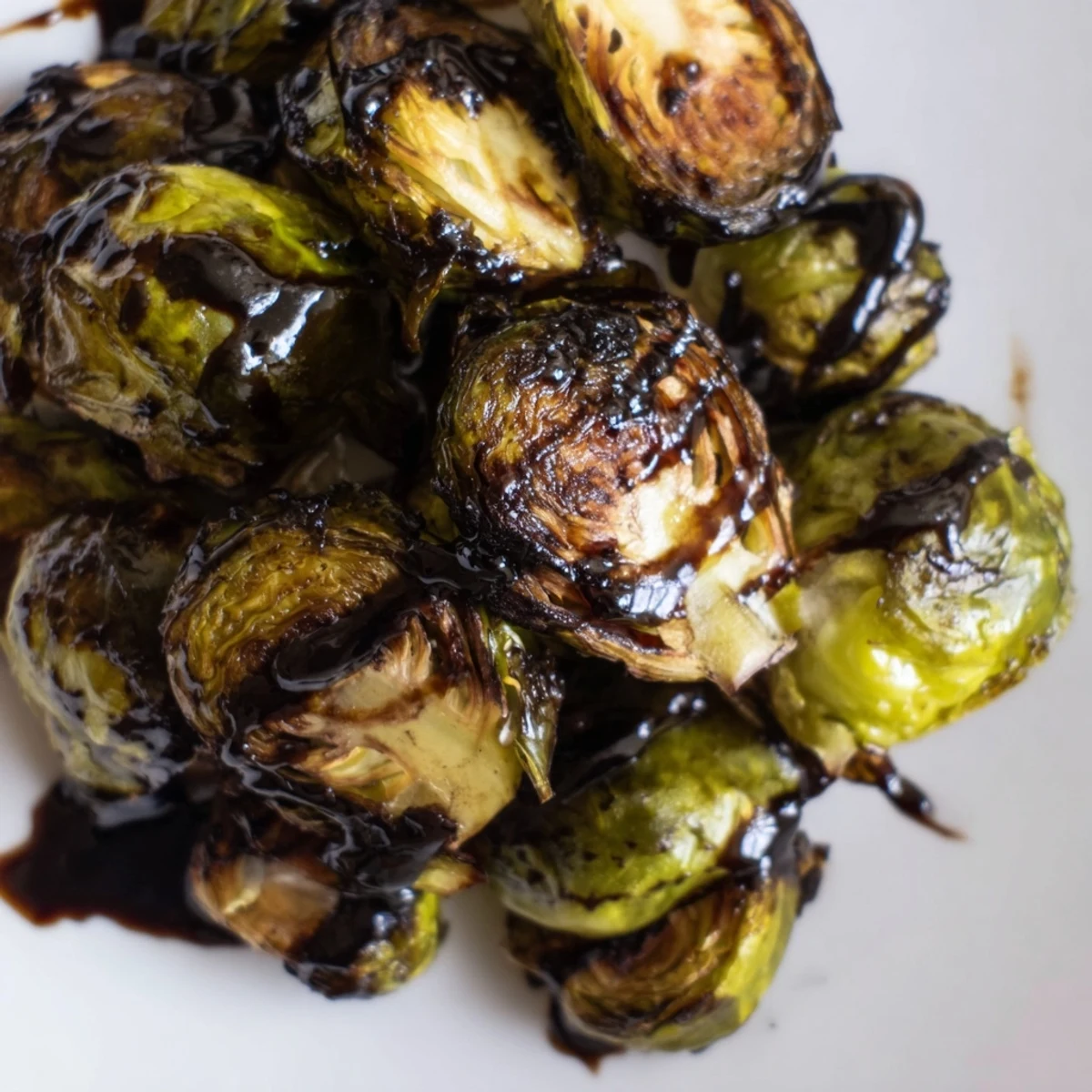 Golden brown Roasted Brussels Sprouts with Balsamic Glaze Reduction are served warm on a rustic plate.