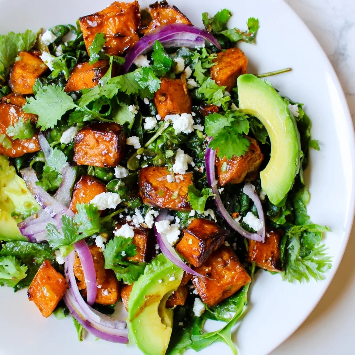 Golden roasted sweet potato salad with caramelized cubes and mixed greens, topped with creamy avocado and a zesty lime dressing.