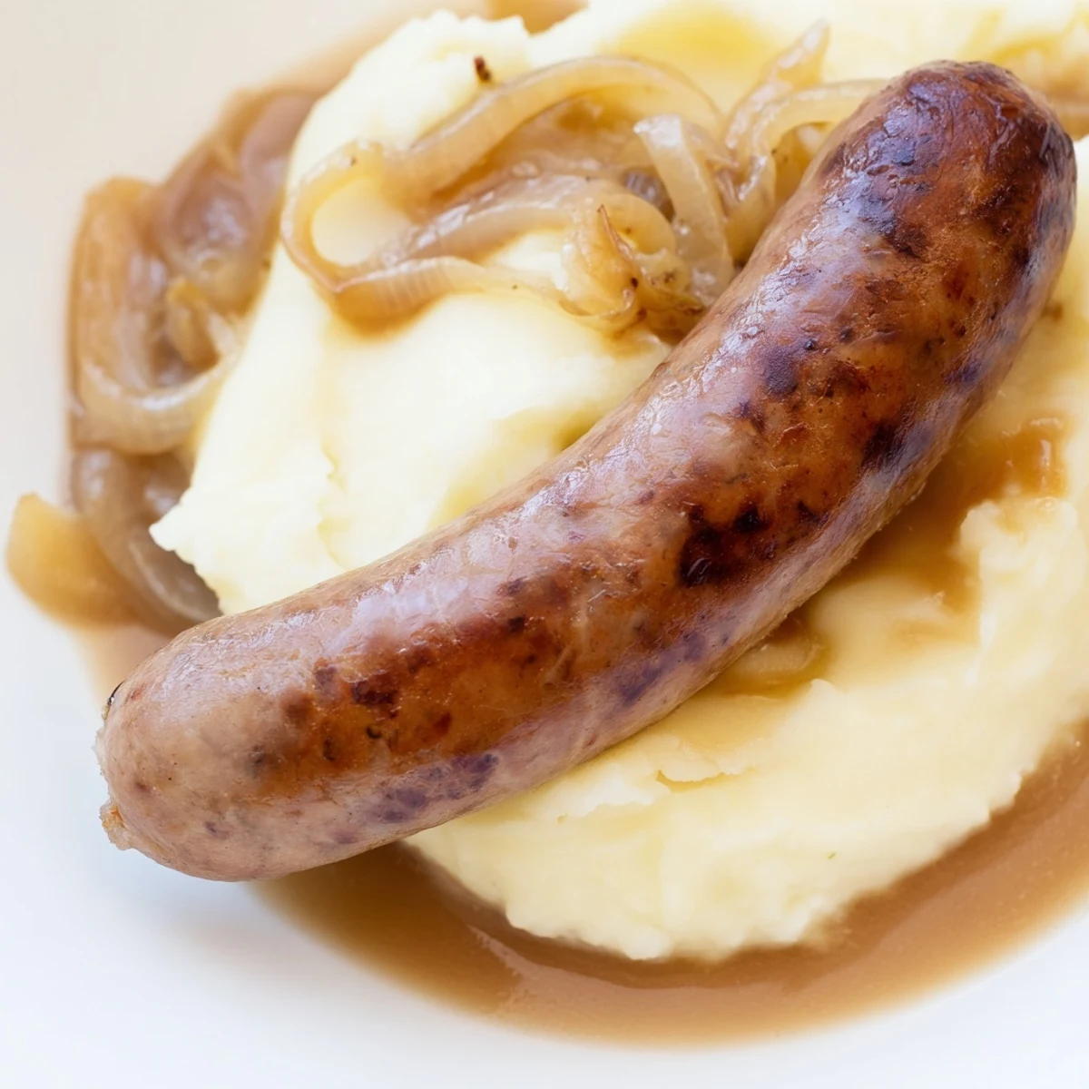 Golden halal sausages over buttery mashed potatoes, drenched in thick onion gravy, ready for a cozy weeknight meal.