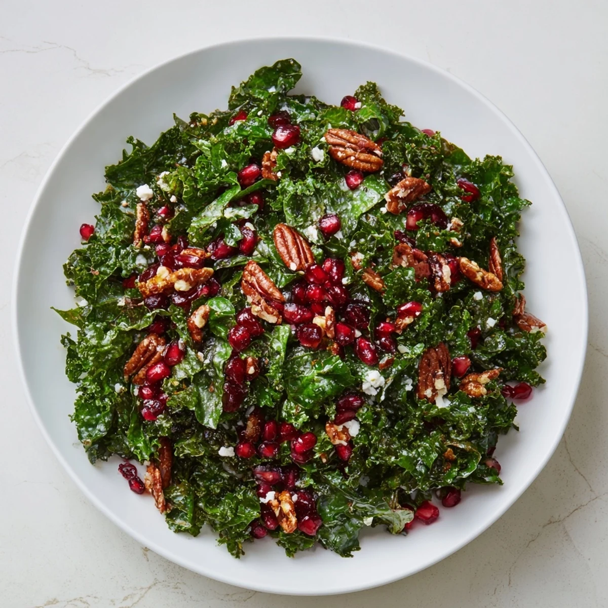 A close-up of Winter Kale Salad with Pomegranate and Pecans, highlighting the crunchy pecans, jewel-like seeds, and a drizzle of tangy dressing.