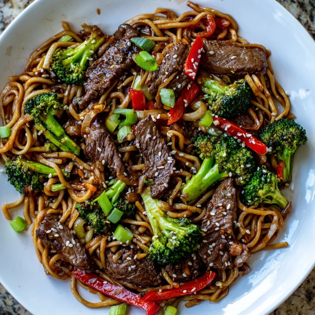Close-up of Beef and Broccoli Lo Mein with Sesame noodles coated in glossy sauce, garnished with sesame seeds and green onions.
