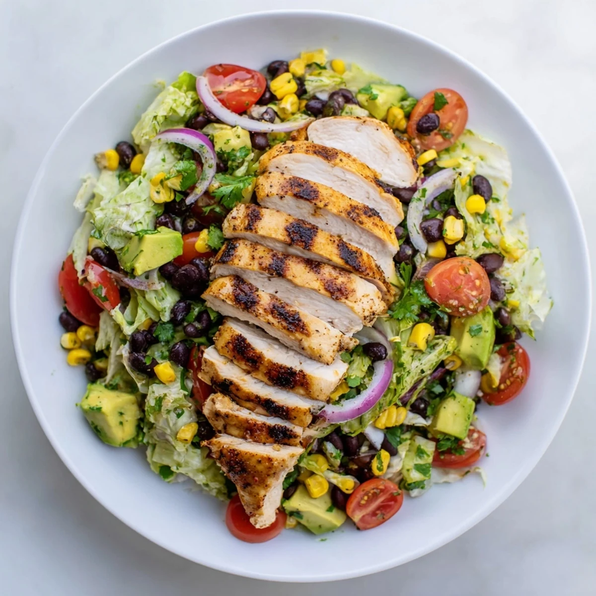 Sliced grilled chicken rests on fresh Southwest Chicken Salad with Lime Dressing, surrounded by black beans and creamy avocado chunks.