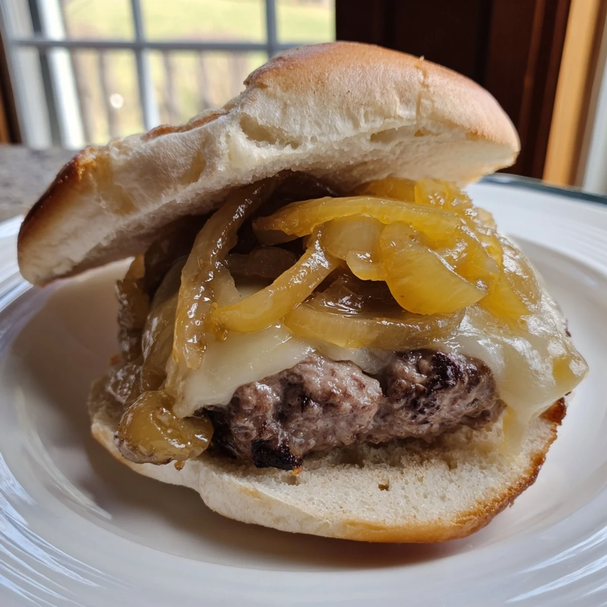 Sizzling beef burger with caramelized onions and melted Swiss cheese sits on a toasted bun beside crisp lettuce and fresh tomato slices.