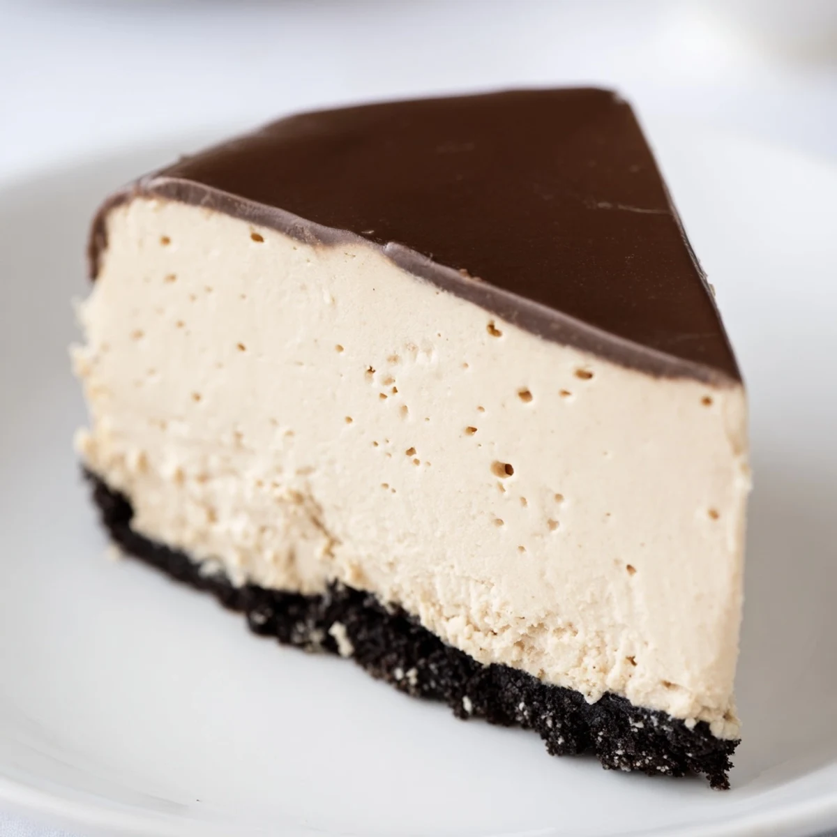 Irish Cream Cheesecake with Chocolate Ganache is displayed whole with a shiny ganache topping on a rustic wooden table.