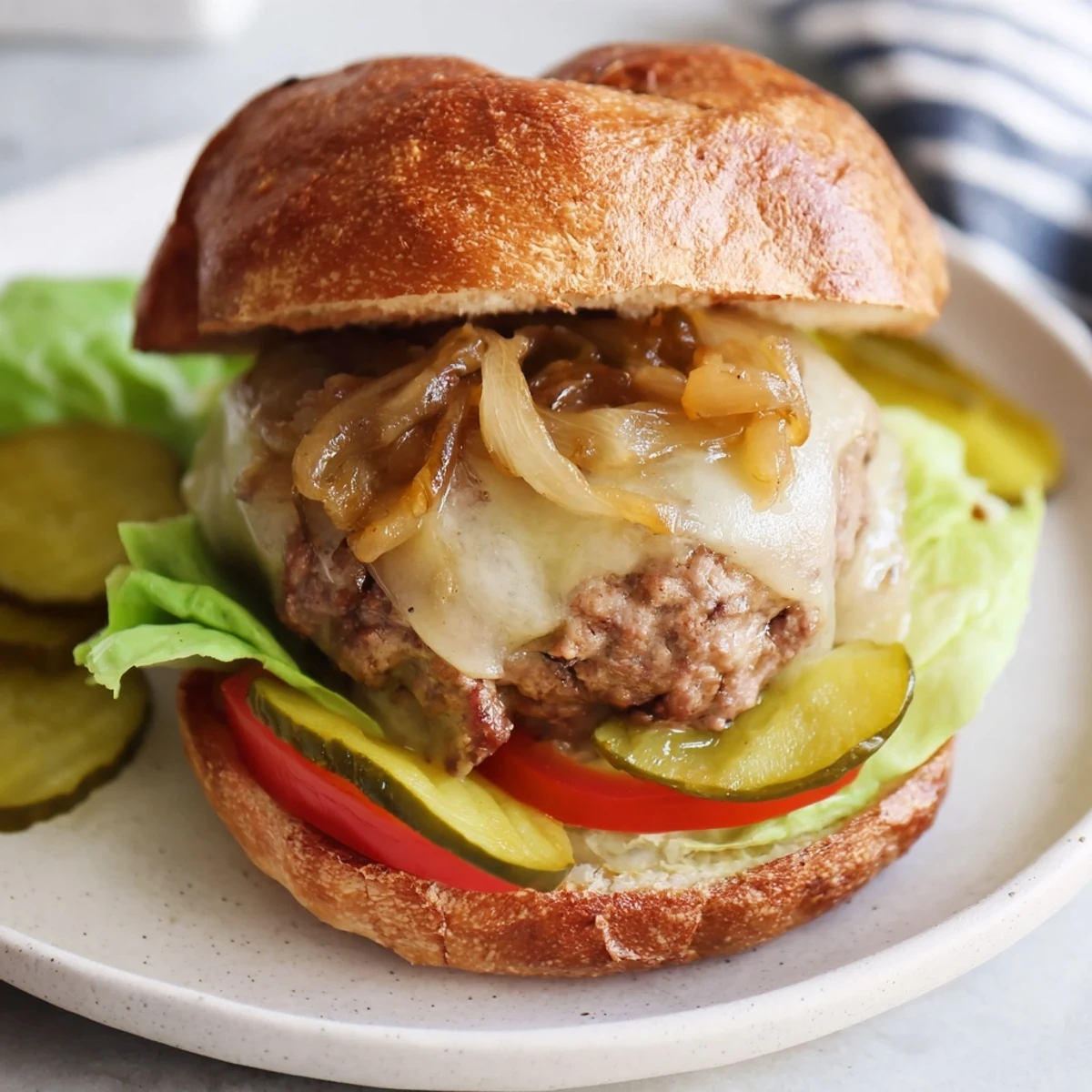 Served on a plate with pickles, this Beef Burger with Caramelized Onions and Swiss looks delicious.