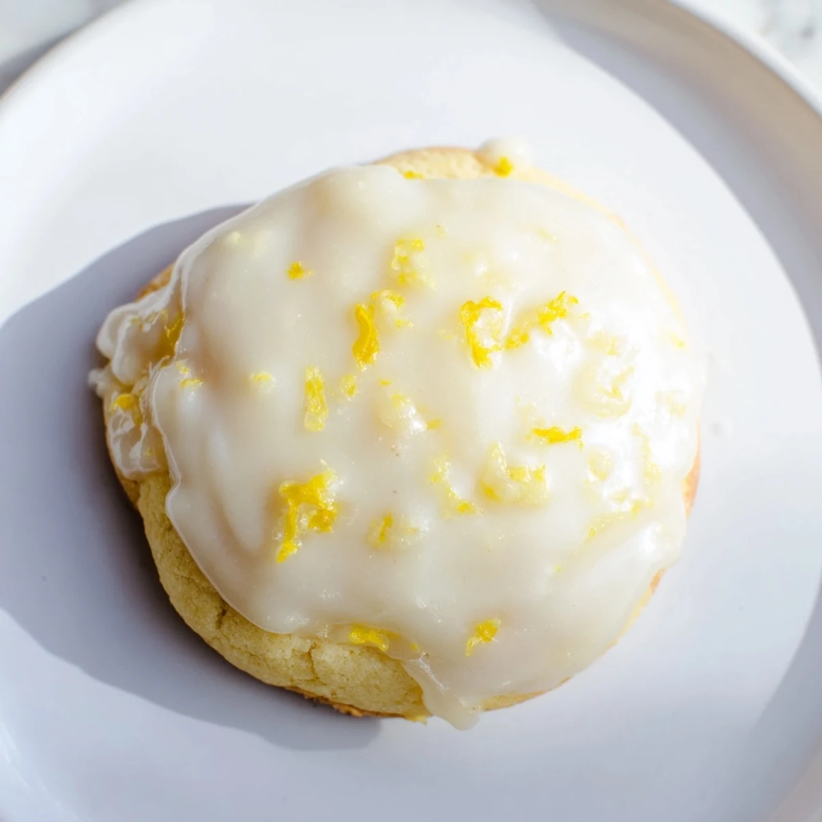 Golden Lemon Ricotta Cookies with Glaze sit on a white plate beside fresh lemons and a sprig of mint.