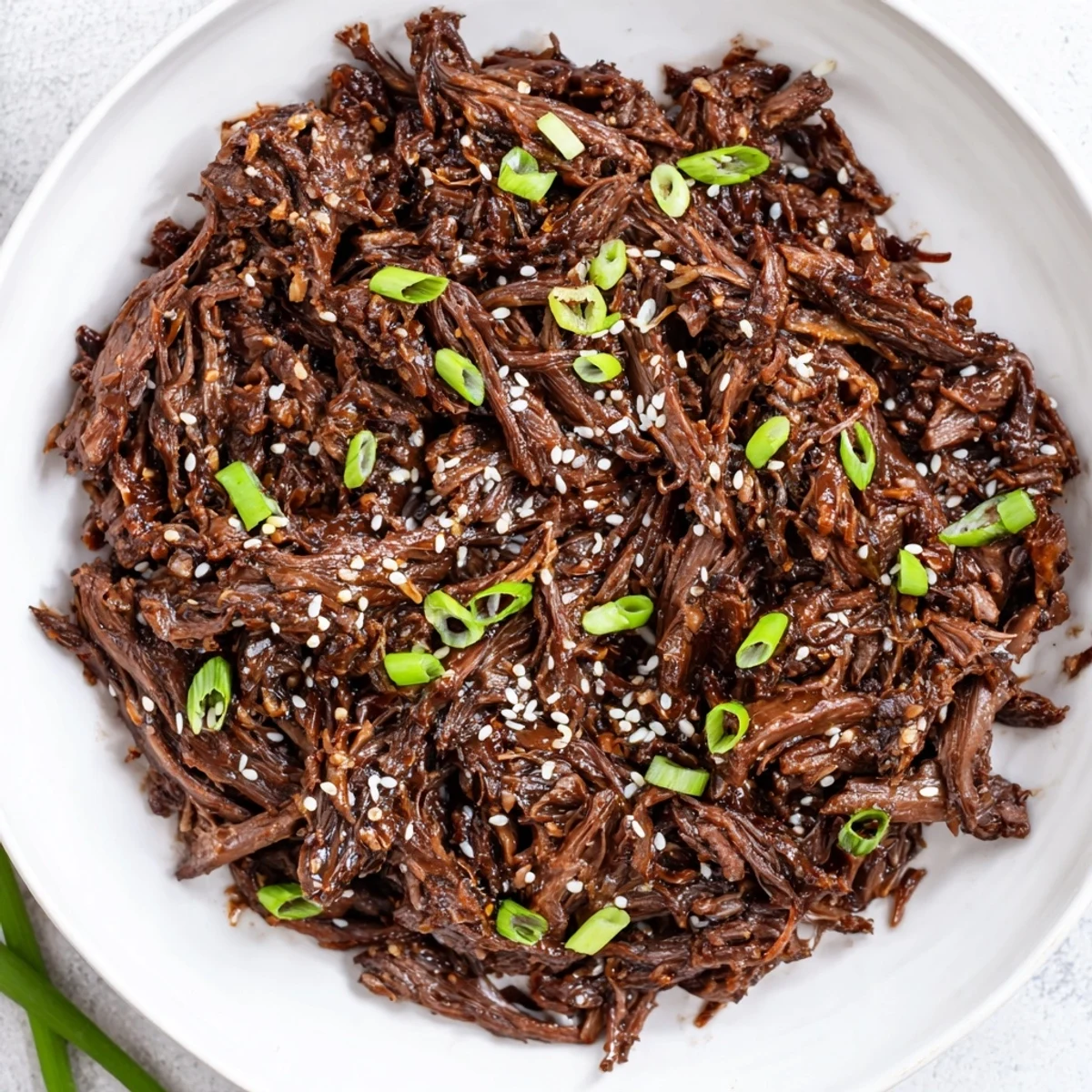 Fork-tender slow cooker Korean beef on a plate with rice and kimchi, garnished with sesame seeds and sliced chili.