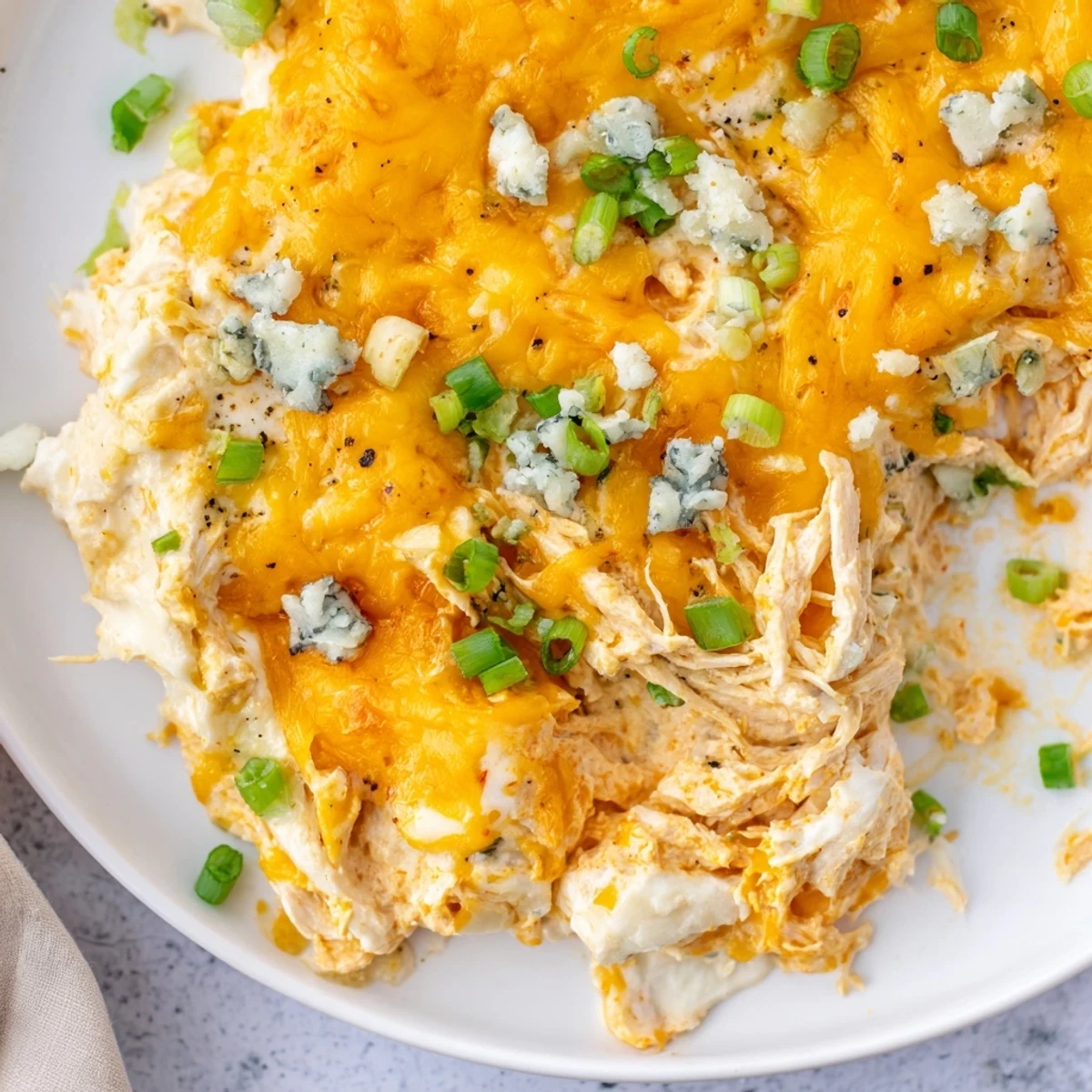 A close-up view of creamy Keto Buffalo Chicken Dip, featuring shredded chicken and buffalo sauce with a bubbly, golden-brown cheese crust from the oven.