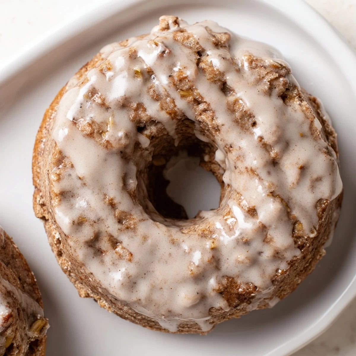 Golden brown Baked Banana Bread Donuts are arranged on a white plate with ripe banana slices.