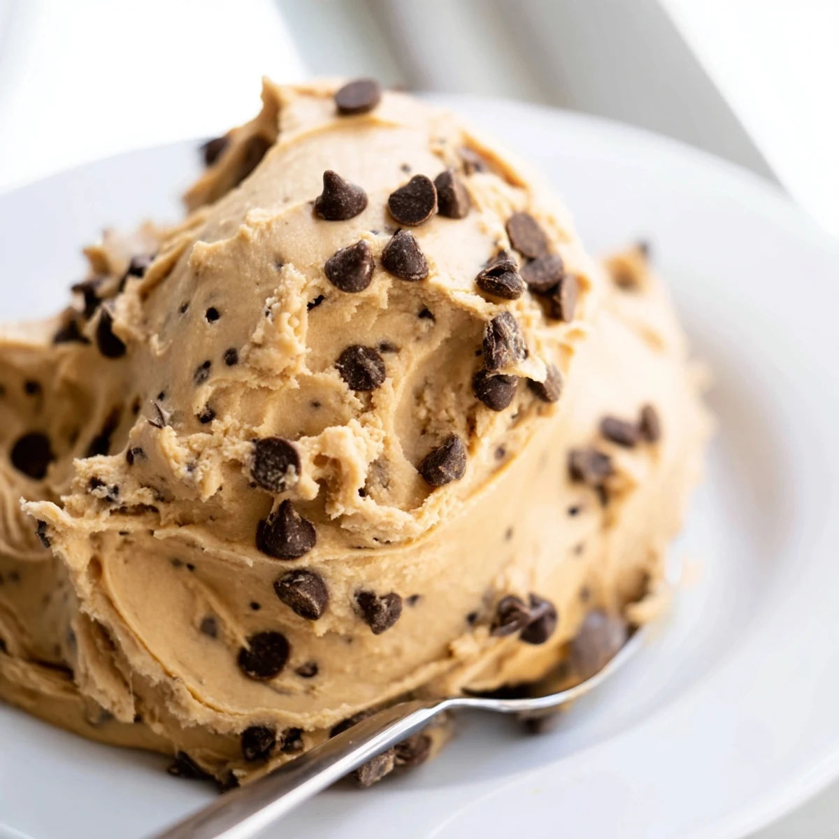 A bowl of creamy Cookie Dough Frosting topped with mini chocolate chips on a wooden table.