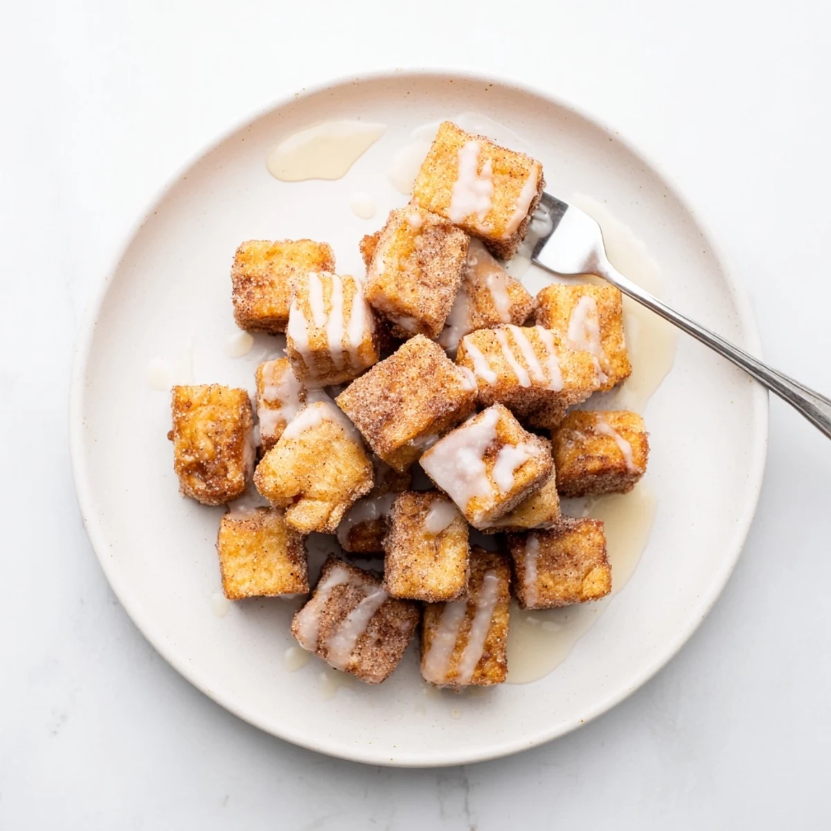 Close-up of fluffy Cinnamon Roll French Toast Bites dusted with cinnamon sugar and glazed.