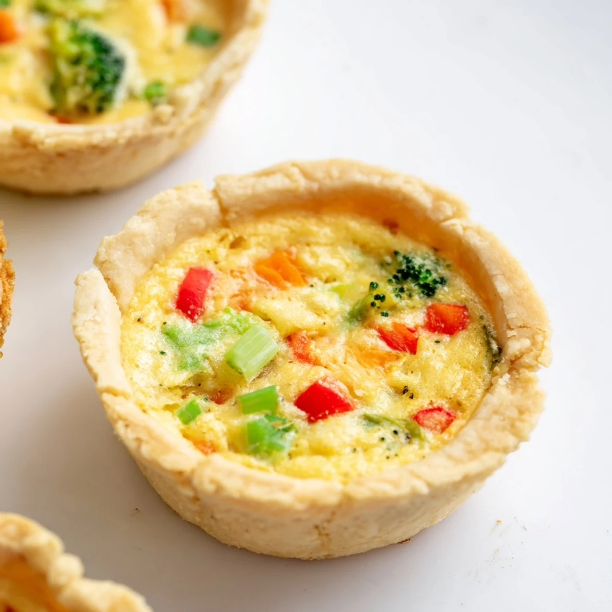 A close-up of a sliced vegan mini quiche showing tender chickpea filling and vibrant spinach, bell peppers, and broccoli inside.