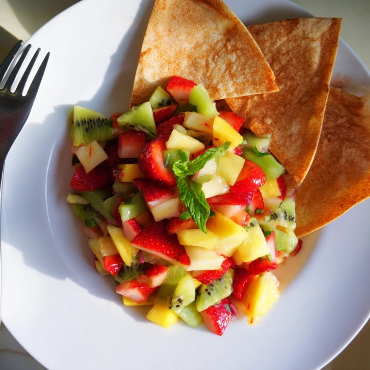 Close-up of Fruit Salsa With Cinnamon Sugar Tortilla Chips dipping into a colorful mix of strawberries, apples, and mint.