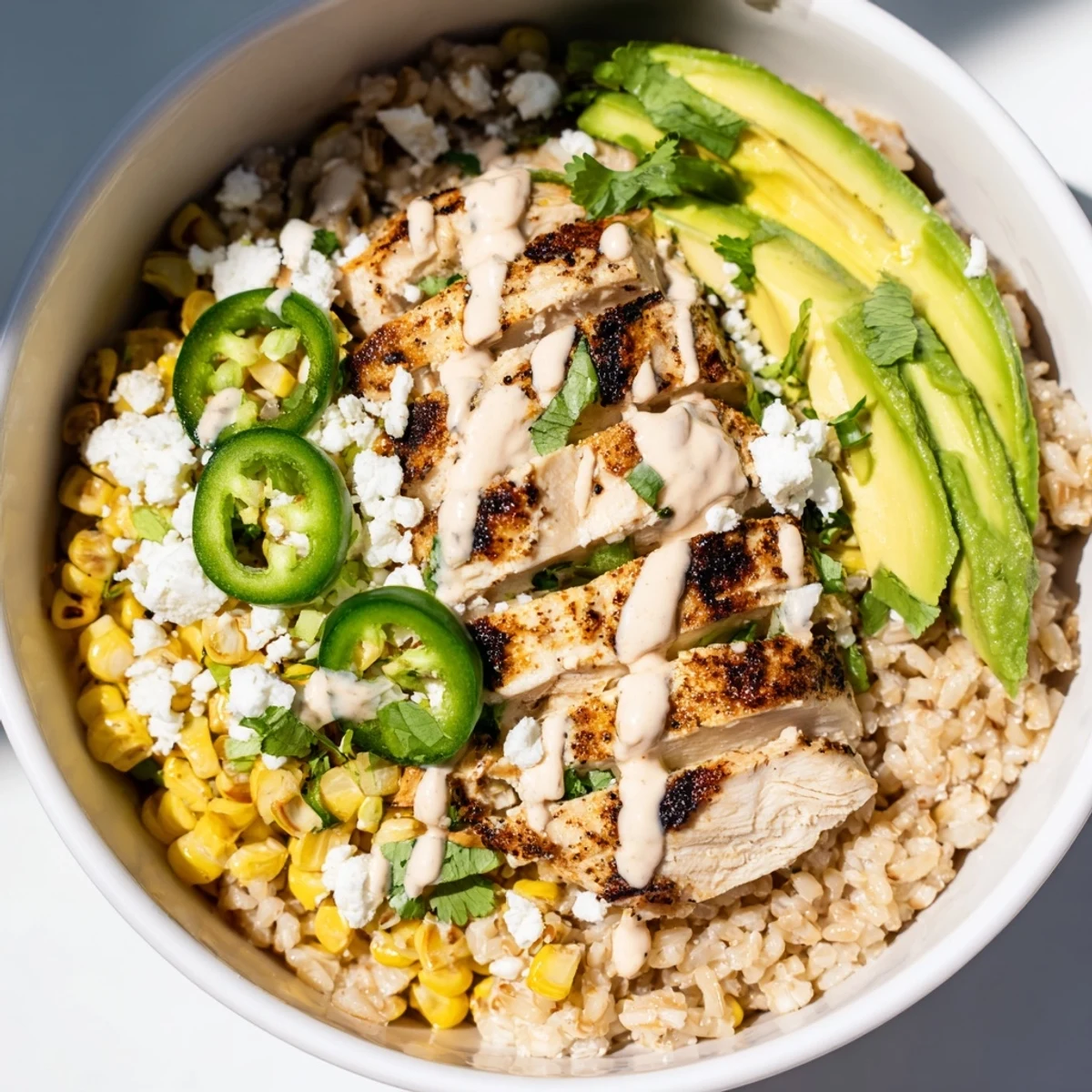 Sizzling grilled chicken and charred corn topping a warm bowl, drizzled with tangy crema and garnished with jalapeño.