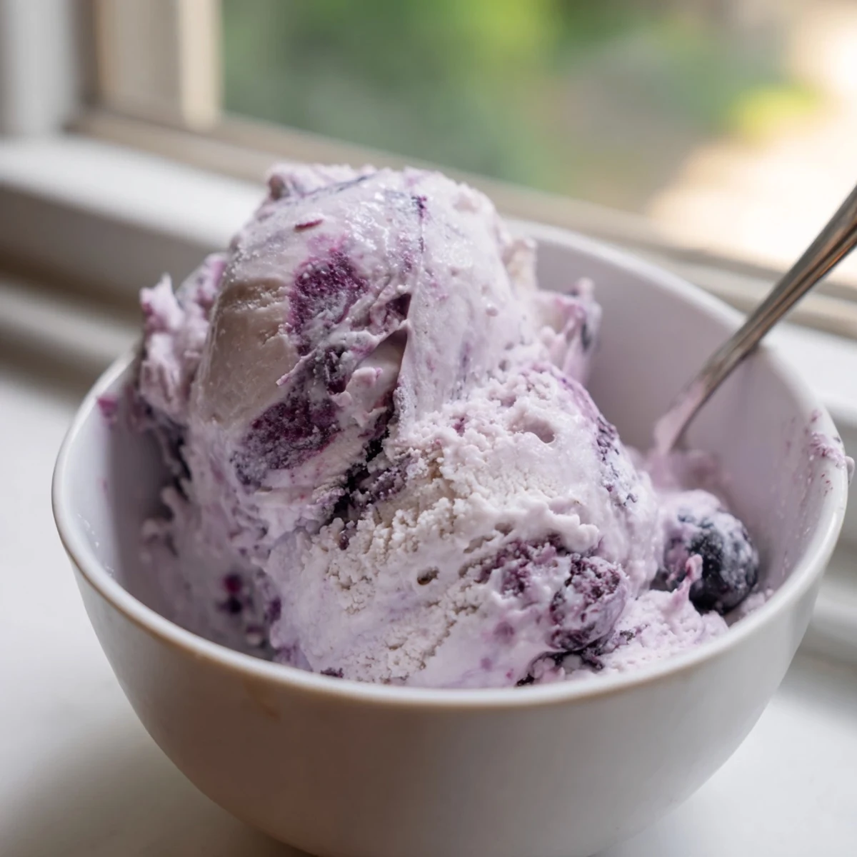 Served in a waffle cone, this high-protein Blueberry Cottage Cheese Ice Cream features swirls of blueberry compote and a drizzle of honey on top.