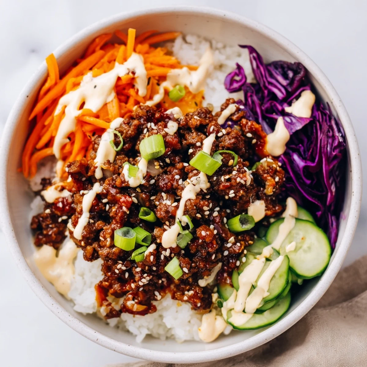 Bright, appetizing Korean Beef Bowl with Spicy Mayo topped with shredded carrots, cucumber, and a spicy mayo swirl for dinner.