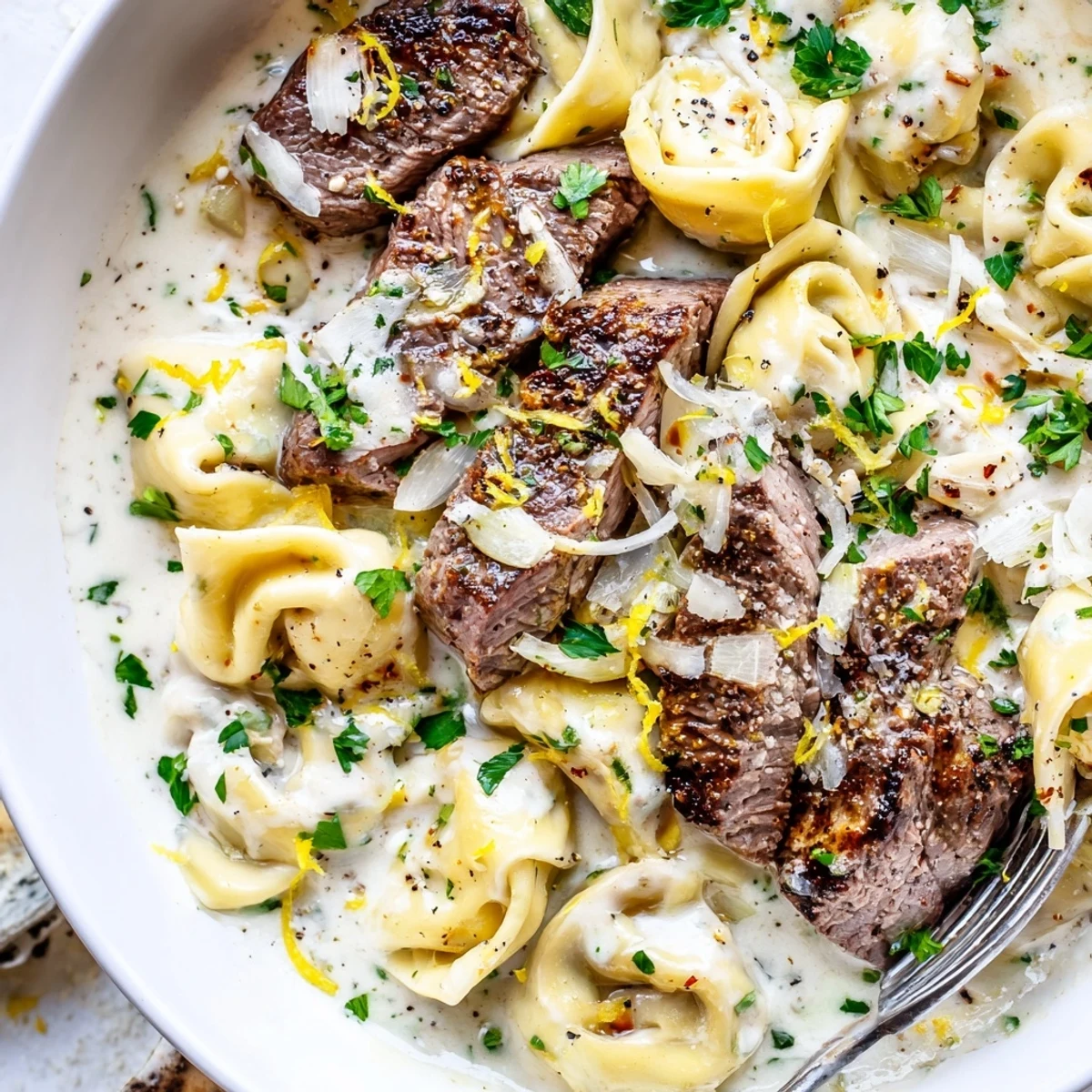 Tender seared steak pieces folded into cheese tortellini swimming in luxurious garlic-herb cream sauce