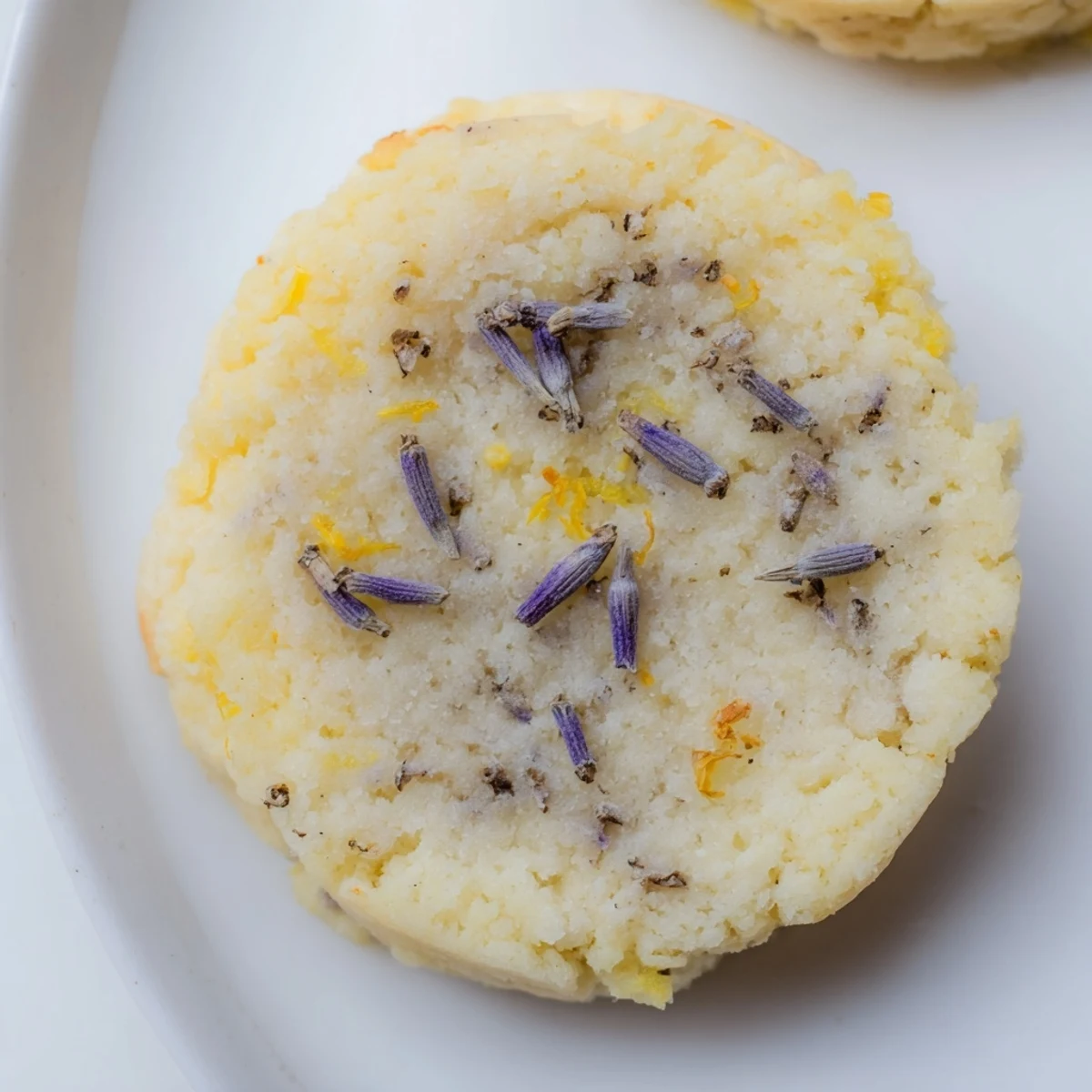 Plate of delicate lemon lavender cookies dusted with powdered sugar alongside a cup of tea