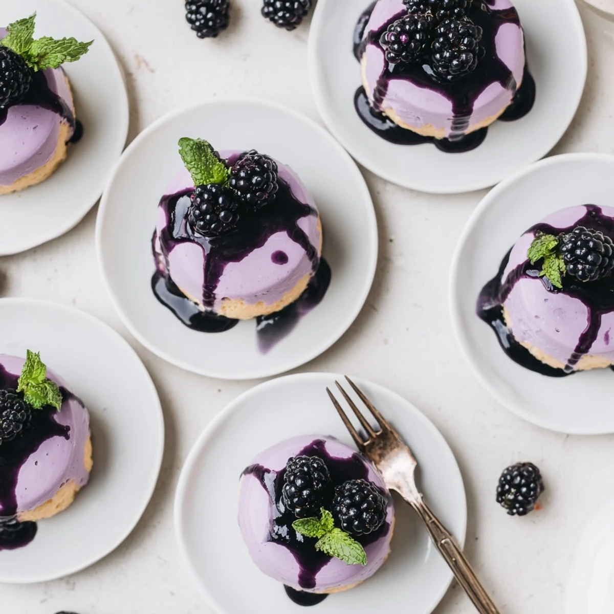 Delicate individual blackberry mousse cakes featuring airy texture atop tender sponge base with shiny topping
