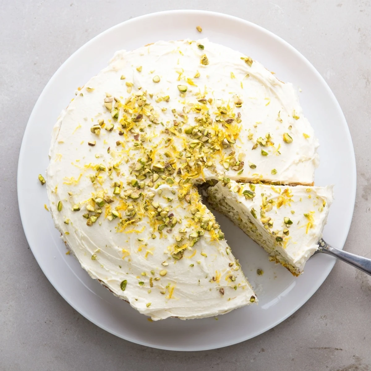 Elegant round cake featuring creamy mascarpone frosting generously sprinkled with green pistachios over bright lemon layers