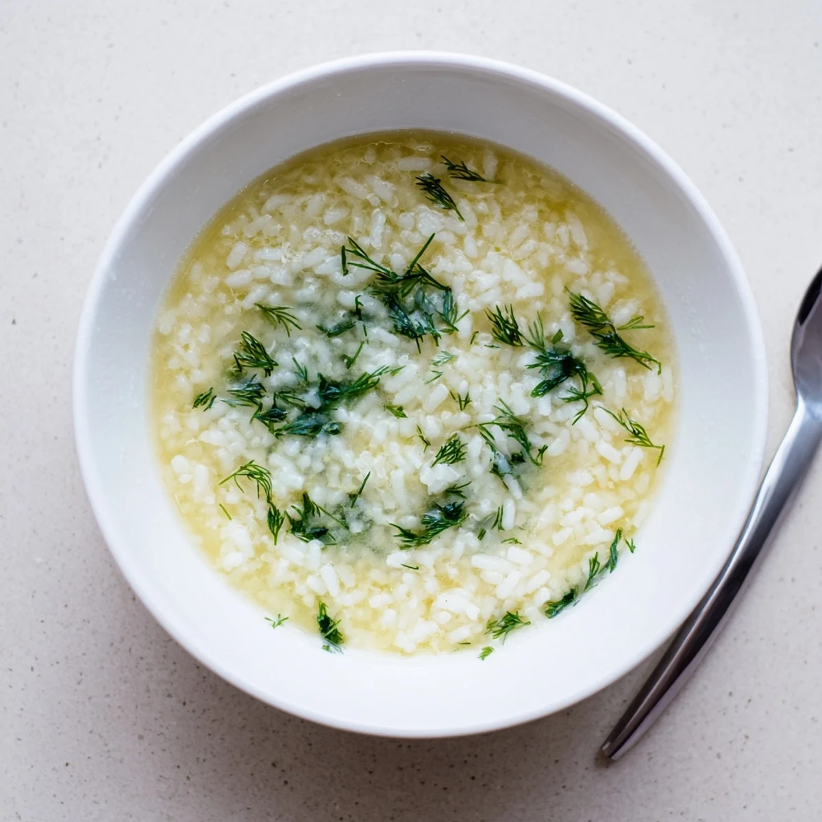 Traditional Avgolemono soup featuring fluffy rice in a bright tangy chicken broth with fresh herbs
