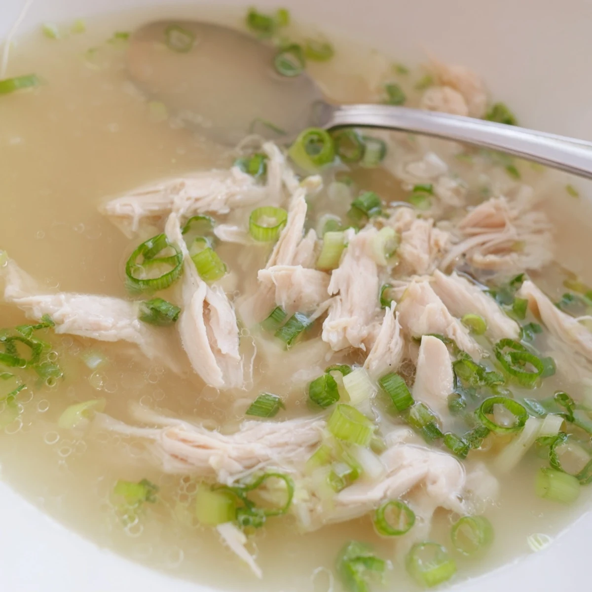 Steaming bowl of Dakgomtang Korean chicken soup garnished with fresh green onions and served alongside dipping sauce