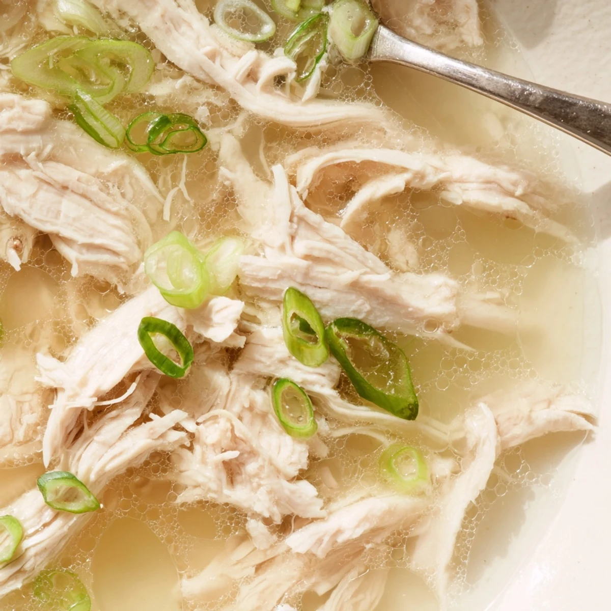 Golden broth of Dakgomtang Korean chicken soup with tender shredded meat and sliced scallions in white bowl