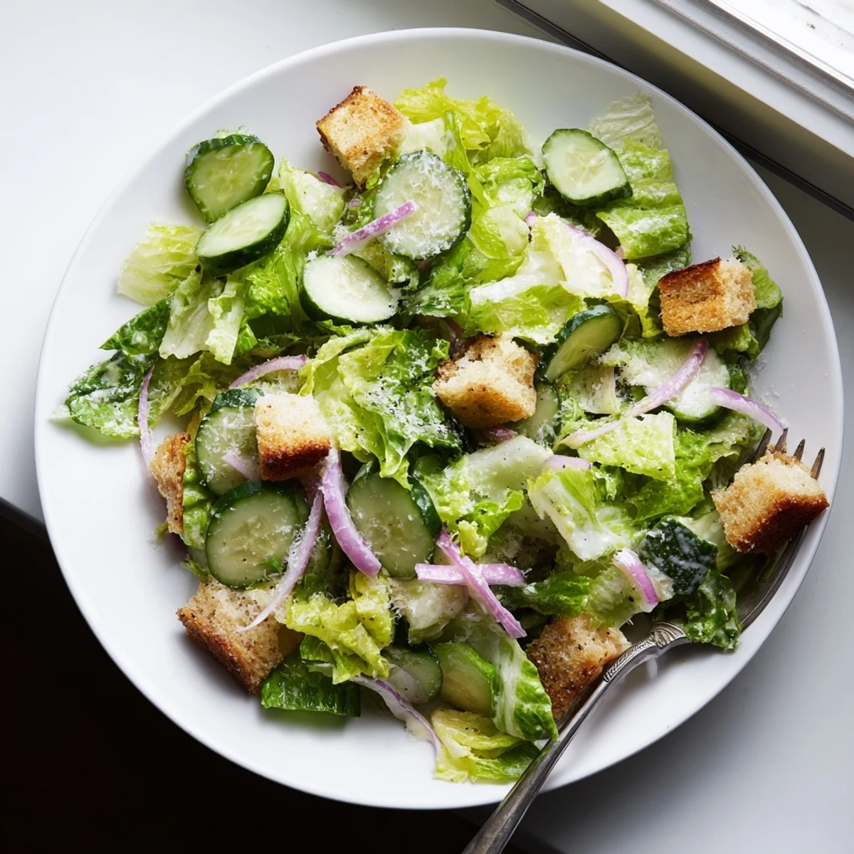 Vibrant cucumber Caesar salad with romaine lettuce, golden toasted croutons, and tangy homemade dressing topped with shaved Parmesan