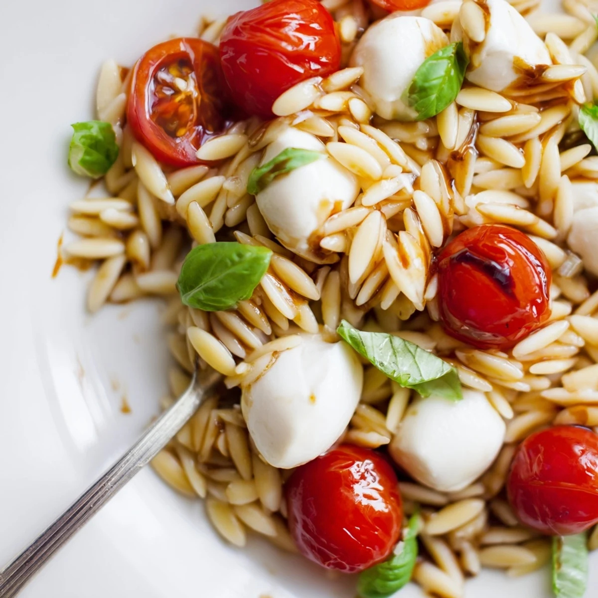 Light and refreshing Caprese orzo pasta salad mounded in a rustic bowl with juicy red tomato halves and creamy white mozzarella