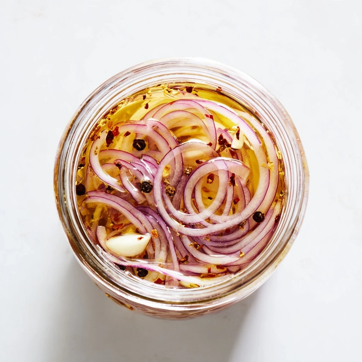 Mason jar showcasing translucent red onion rings steeped in spicy honey vinegar infusion