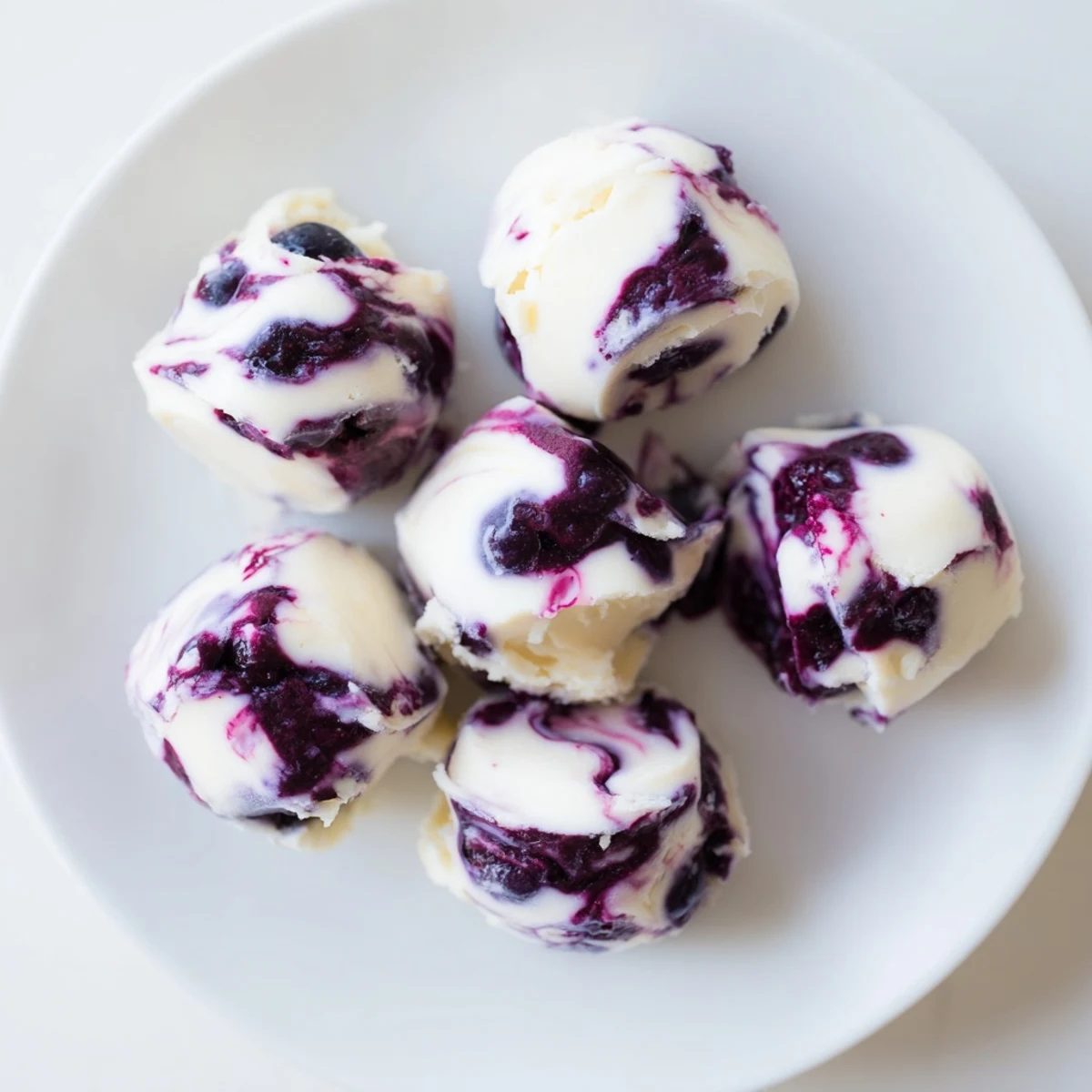Golden blueberry swirl yogurt bites arranged on a white plate showing vibrant purple streaks through creamy frozen Greek yogurt squares