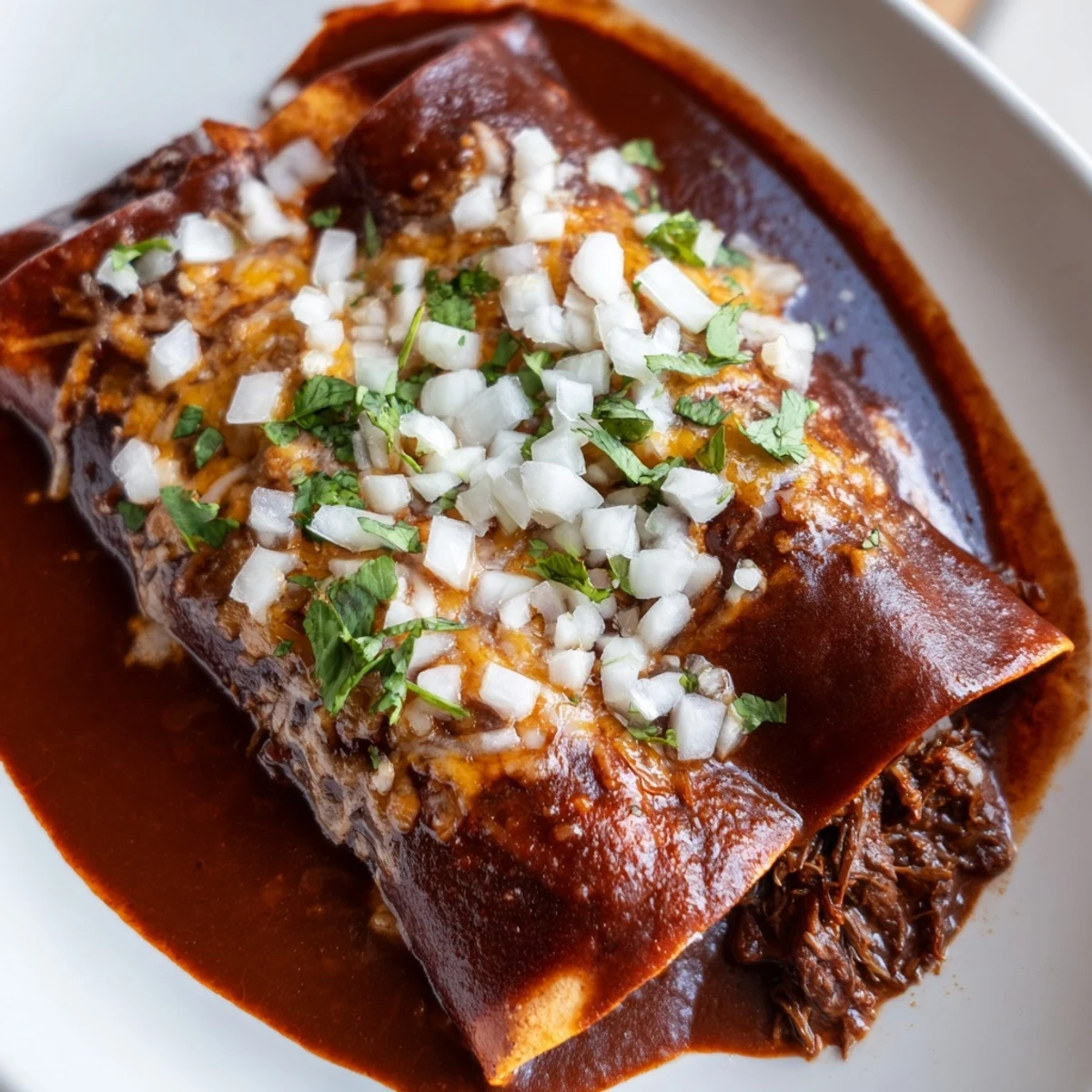 Golden birria enchiladas baking with melted Oaxaca cheese and rich consommé sauce