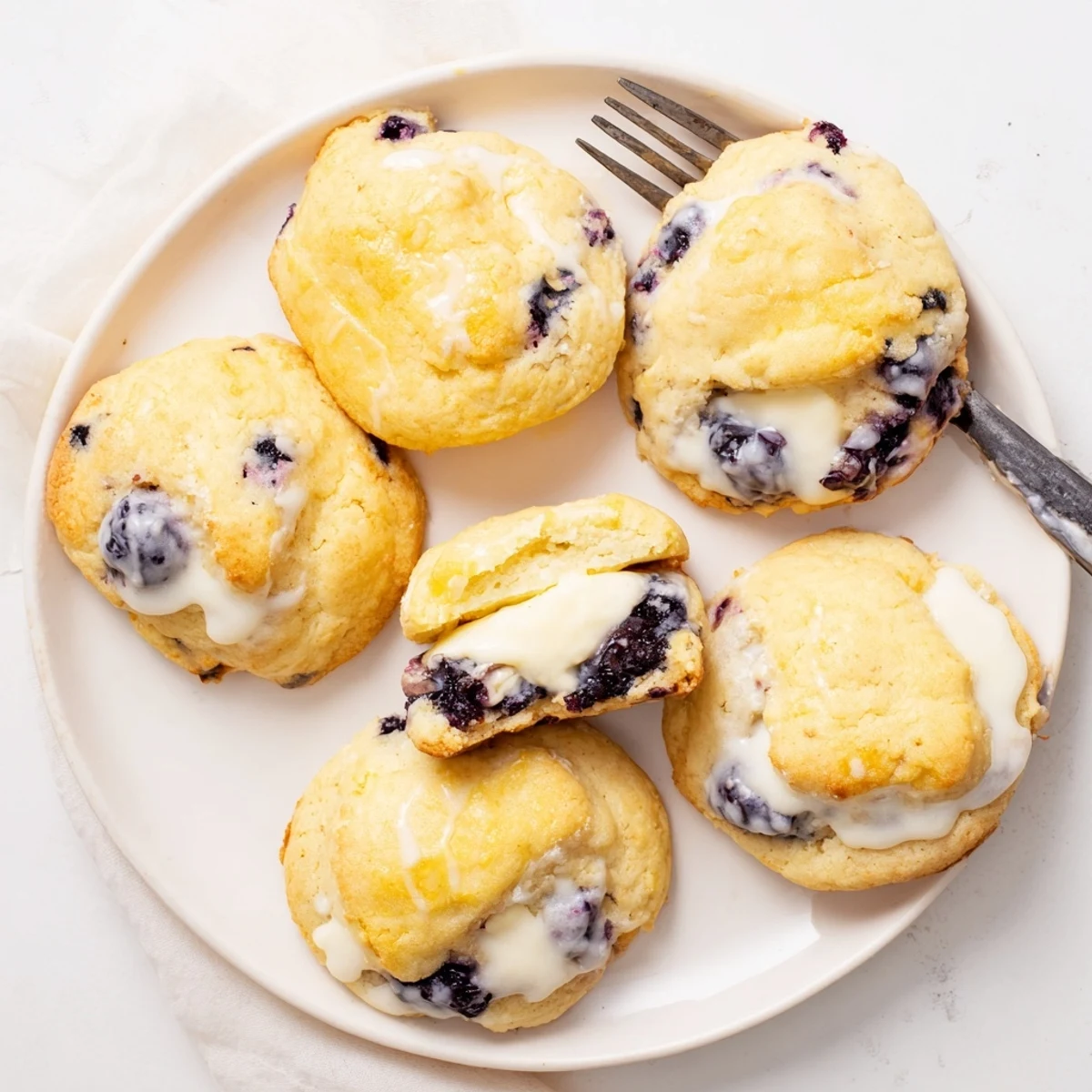 Soft lemon blueberry cheesecake cookies with creamy centers and plump purple berries on a white plate