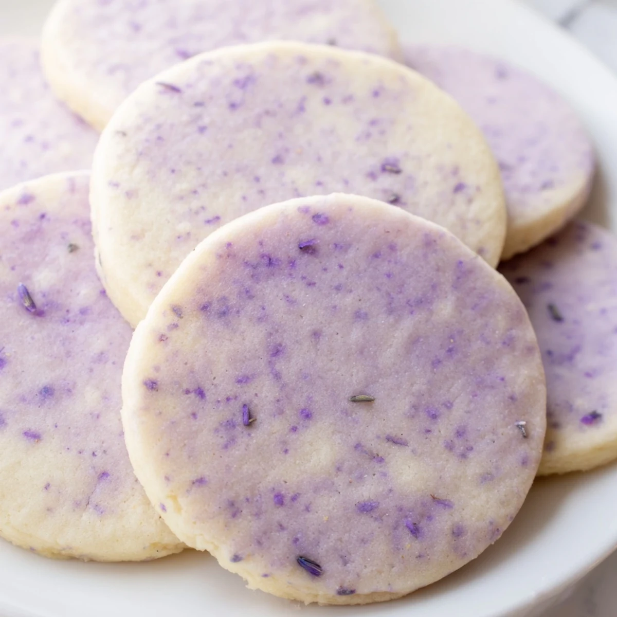 Buttery lilac sugar cookies arranged on a white plate with scattered edible blossoms