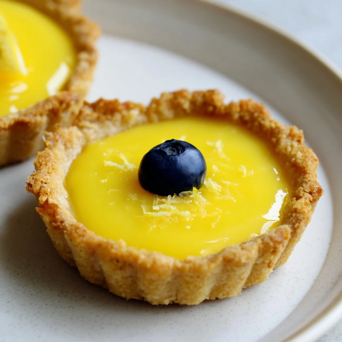 Golden mini vegan lemon tarts topped with fresh berries on a white serving plate