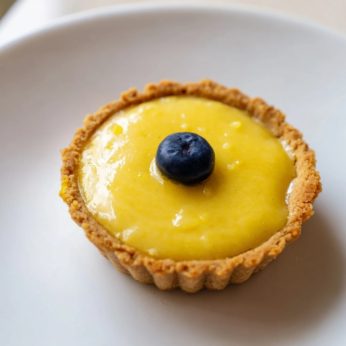 Mini vegan lemon tarts with glossy yellow custard filling garnished with lemon zest curls