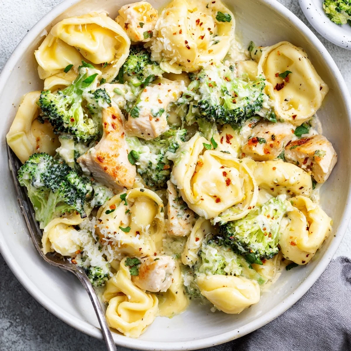 Skillet steaming with garlic cream, tender chicken—Creamy Garlic Parmesan Tortellini Chicken Broccoli Recipe.