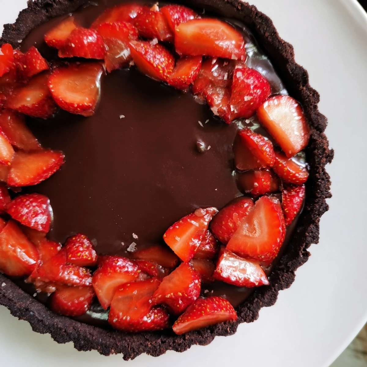 Sliced Dark Chocolate Strawberry Tart chilled on plate, almond crumbs and fork