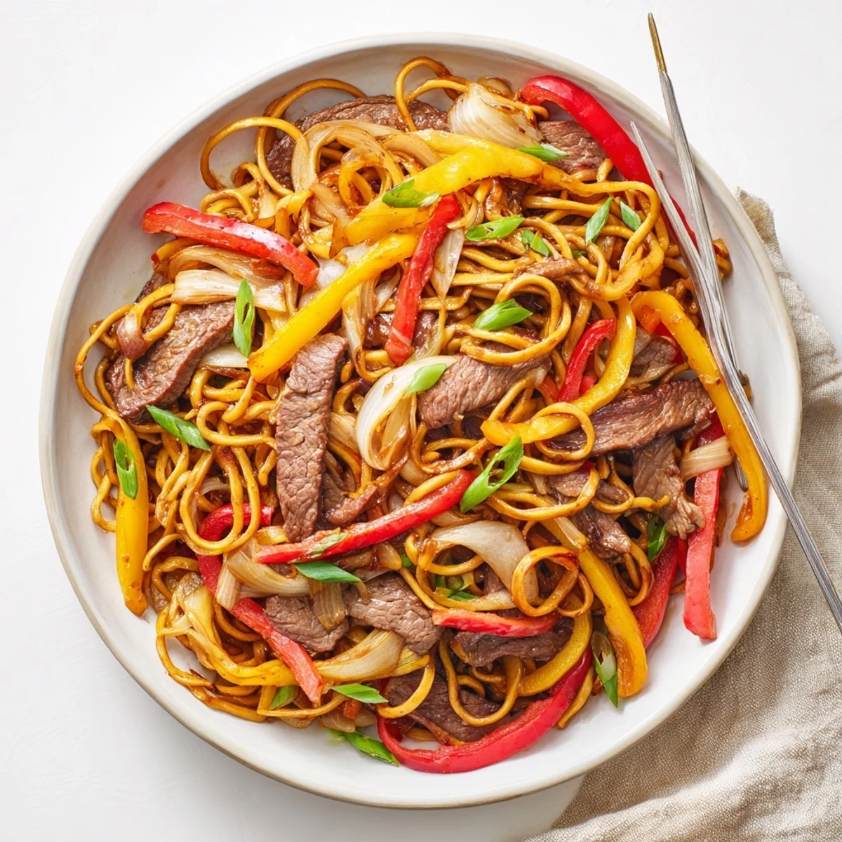 Plate of beef chow mein with peppers and onions tossed in glossy savory sauce