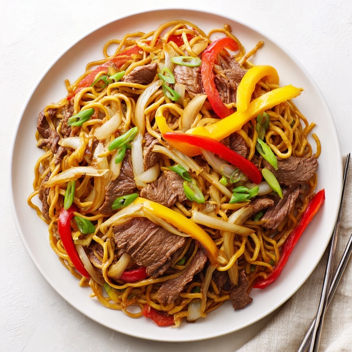 Wok full of sizzling beef chow mein featuring colorful bell peppers and sliced onions