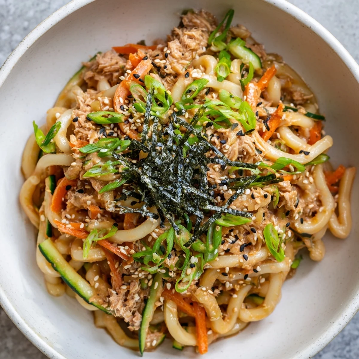 Spicy tuna udon with fresh cucumber carrots and sesame seed garnish