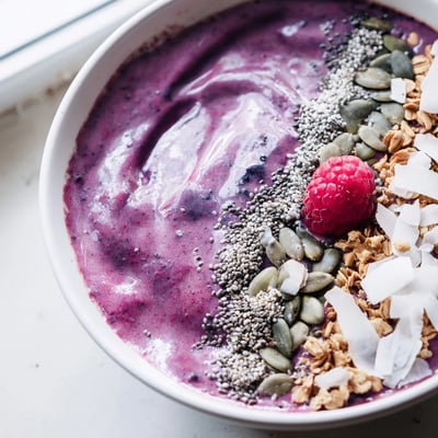 This thick purple smoothie bowl is garnished with pumpkin seeds, chia seeds, and sweet coconut flakes.